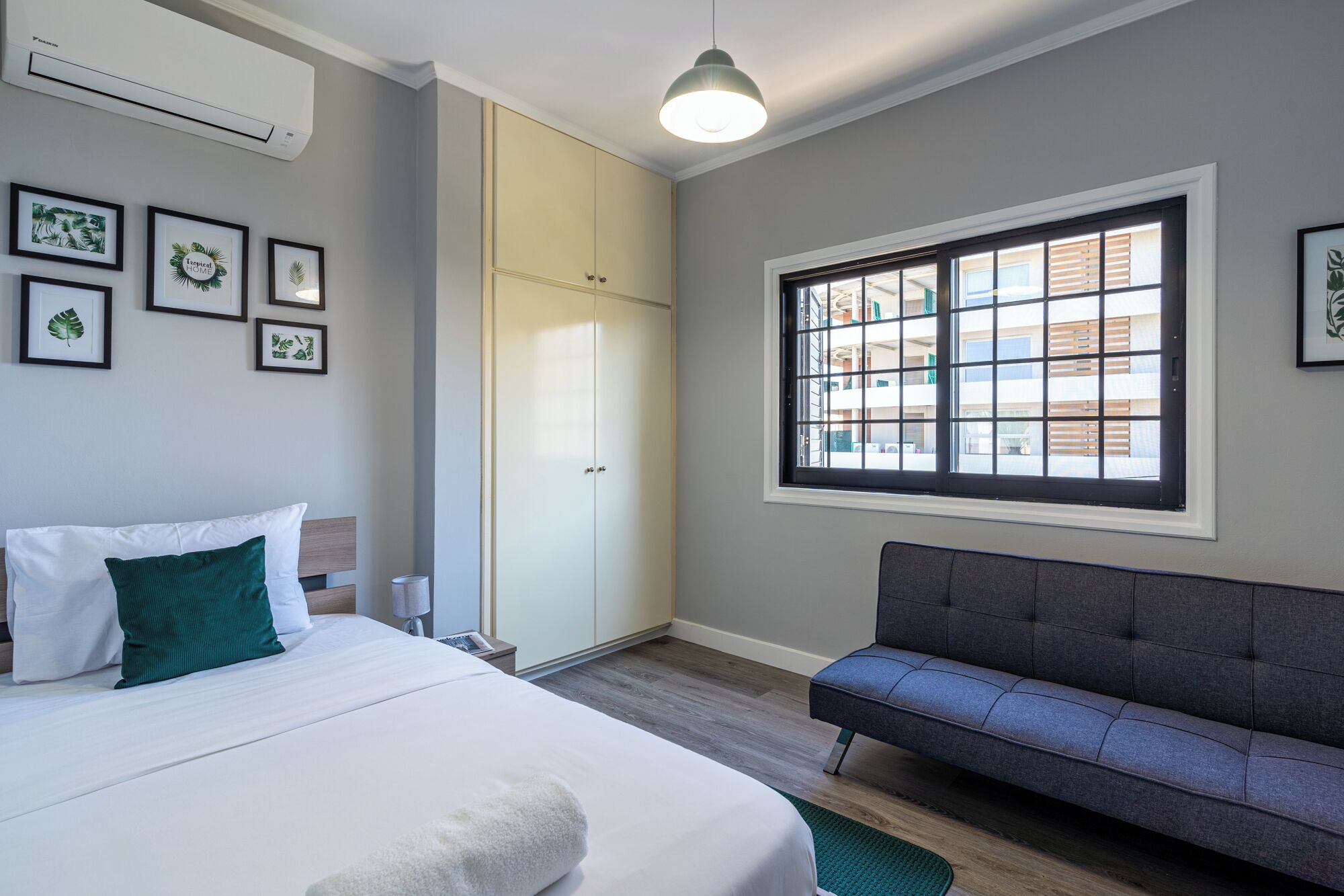 Un dormitorio con cama, sofá, ventana con vistas y cuadros en la pared.