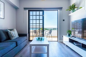 Una sala de estar moderna con sofá, una mesa de centro, televisor y un balcón con mobiliario exterior.