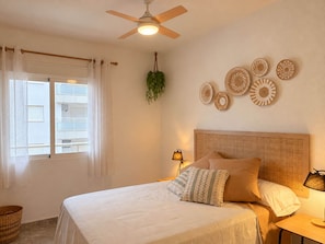 Een slaapkamer met een bed, een plafondventilator, een raam met gordijnen en wanddecoratie.