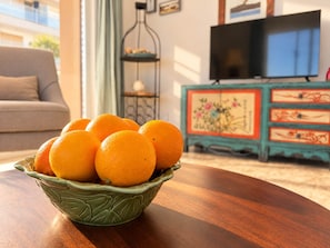 Eine Schüssel Orangen auf einem Holztisch in einem Wohnzimmer mit einer Couch und einem Fernseher im Hintergrund.