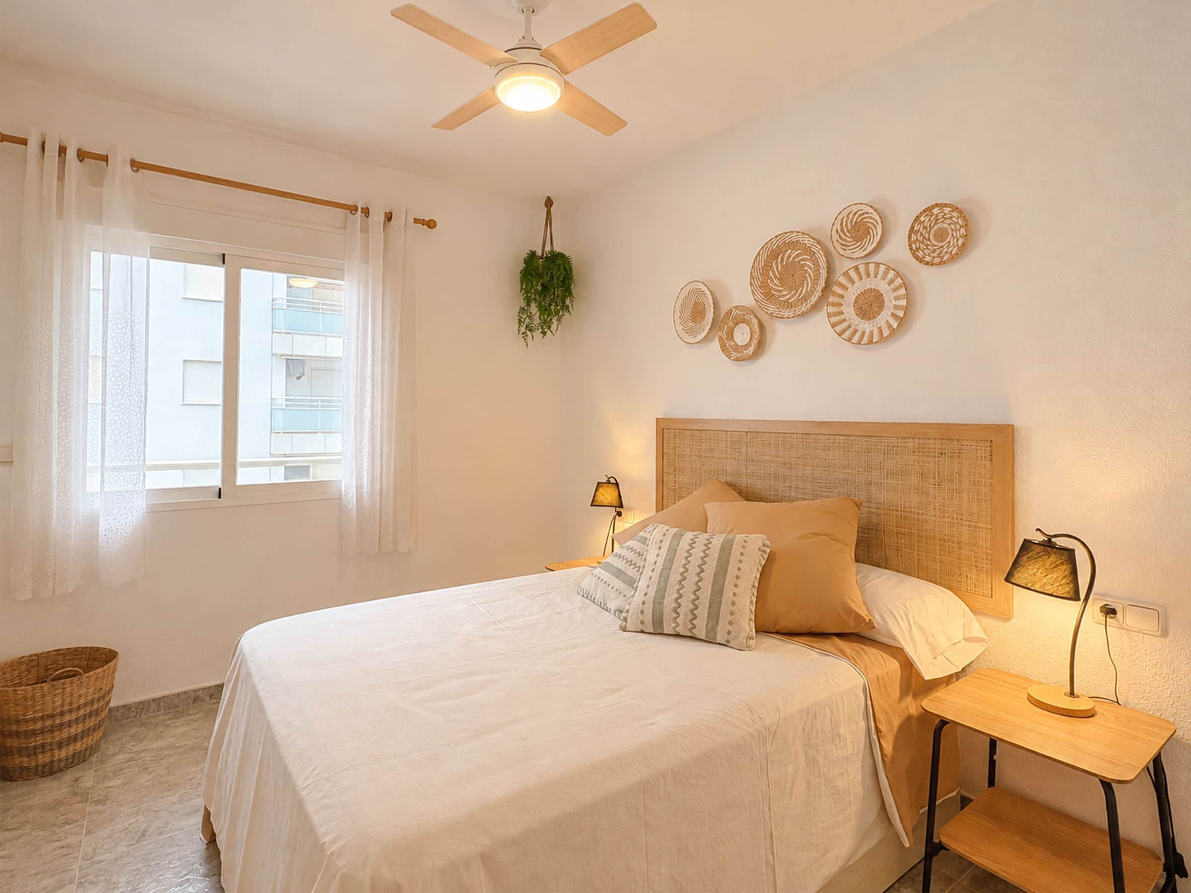 A bedroom with a bed, bedside tables, a ceiling fan, and wall decorations.