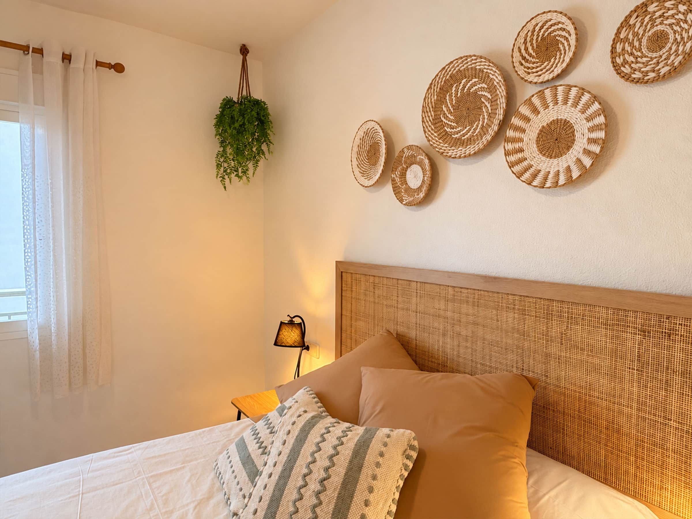 Ein Schlafzimmer mit einem Bett, Kissen, einer Nachttischlampe, einer hängenden Pflanze und Wanddekorationen aus Gewebe.