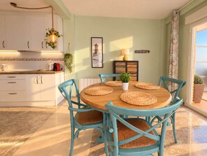 A dining area with a round table, six chairs, and a view of the sea through a window. - Ninomad 02 Beachfront - Near Gandía (Daimús)