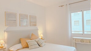 Een slaapkamer met een bed, nachtkastjes, een raam en foto’s aan de muur.