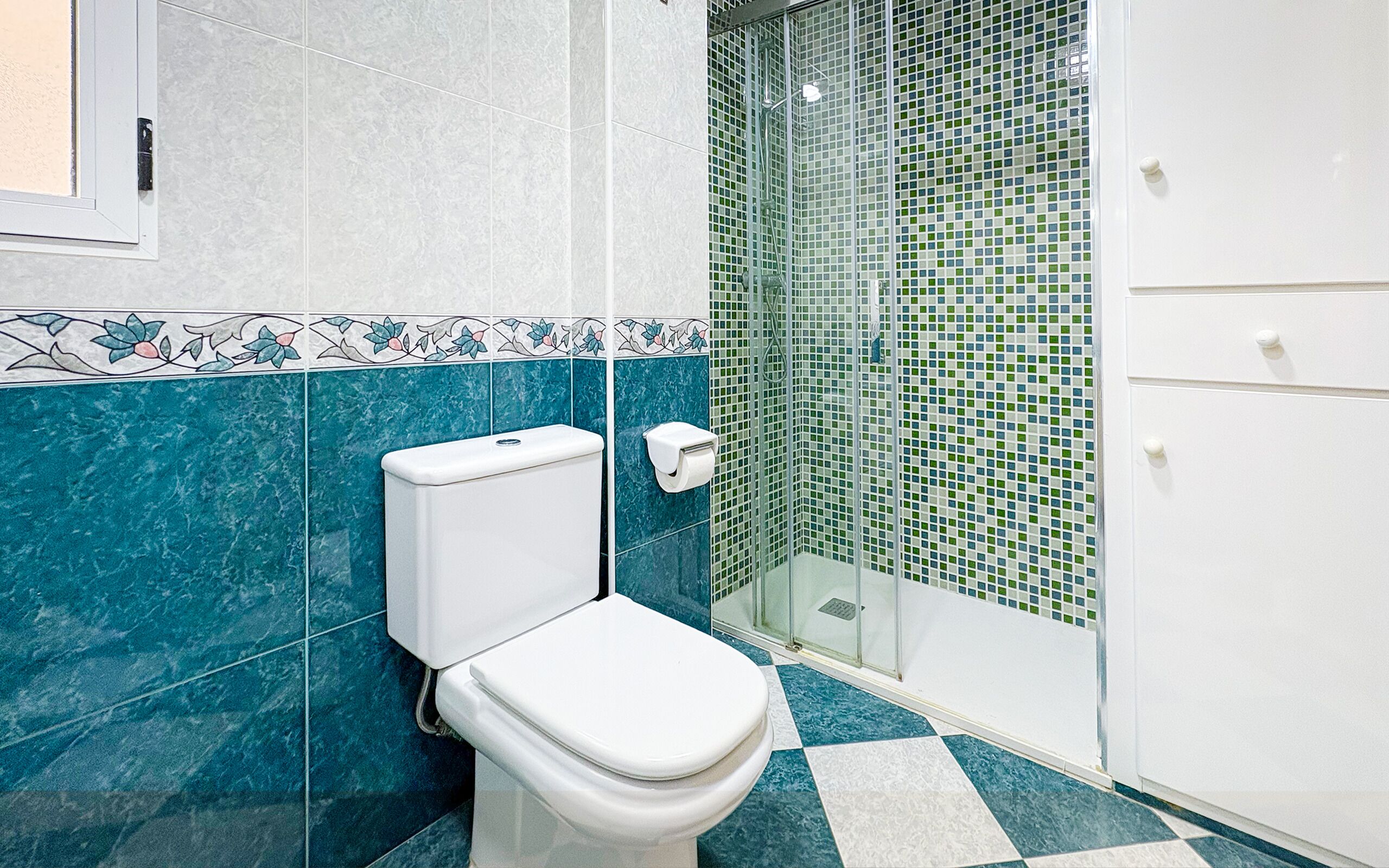 Un baño con inodoro, ducha con puerta de cristal y piso de baldosas.