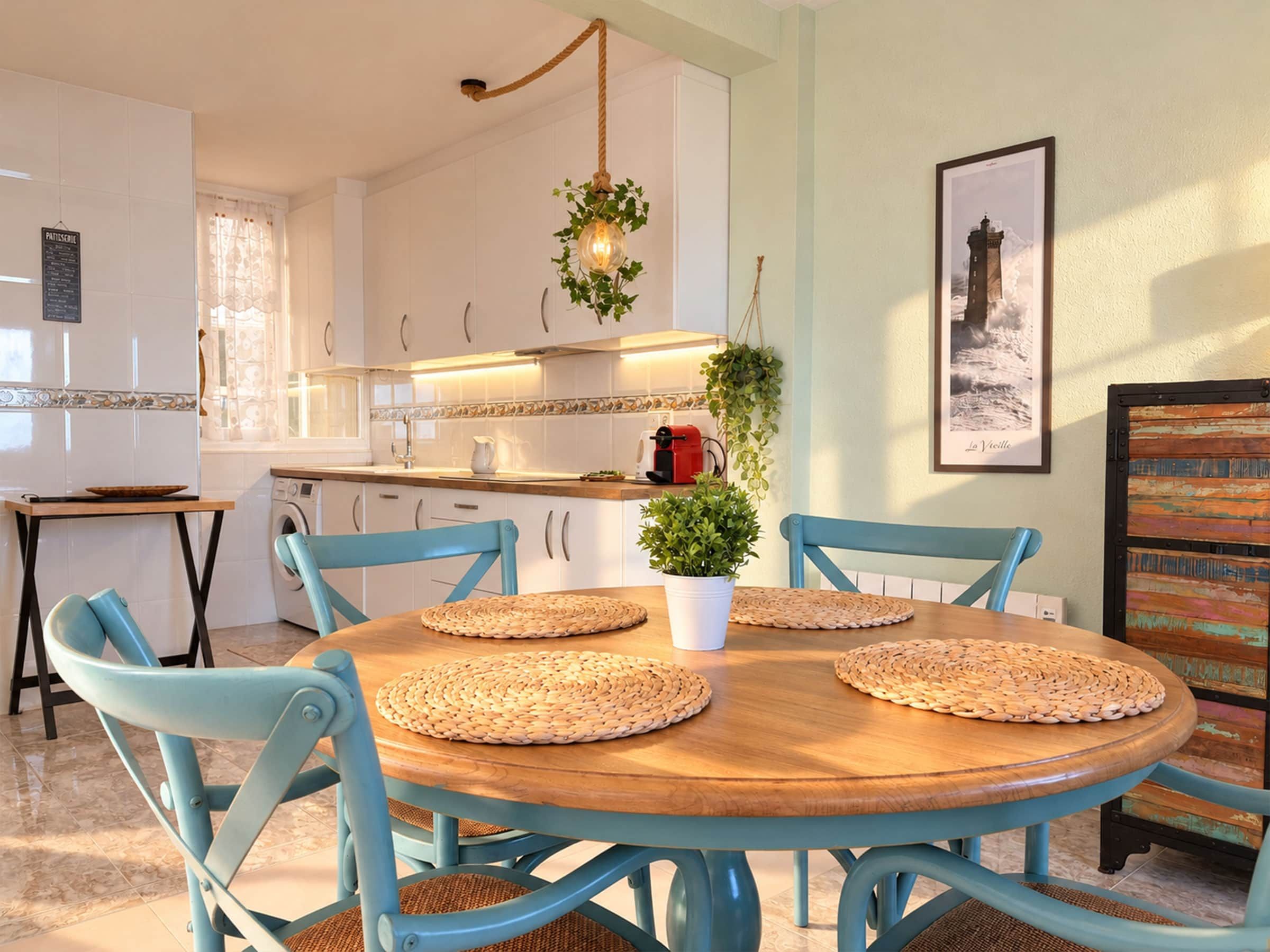 Un coin repas avec une table ronde en bois, des chaises bleues et des sets de table en fibres tressées.