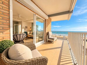 A balcony with wicker furniture, a glass door leading to a living area, and a view of the beach. - Ninomad 02 Beachfront - Near Gandía (Daimús)