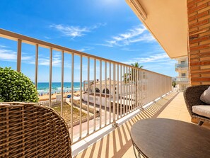 Een balkon met uitzicht op het strand, rieten meubilair en een gebouw met een pannendak.
