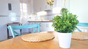 Een keuken met witte kastjes, een houten tafel met een geweven placemat en een potplant.