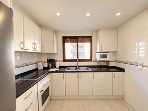 A kitchen with white cabinets, a black countertop, a stainless steel sink, and a microwave. - 04 Caerulea - Sea View Apartment - Daimús (Daimús)