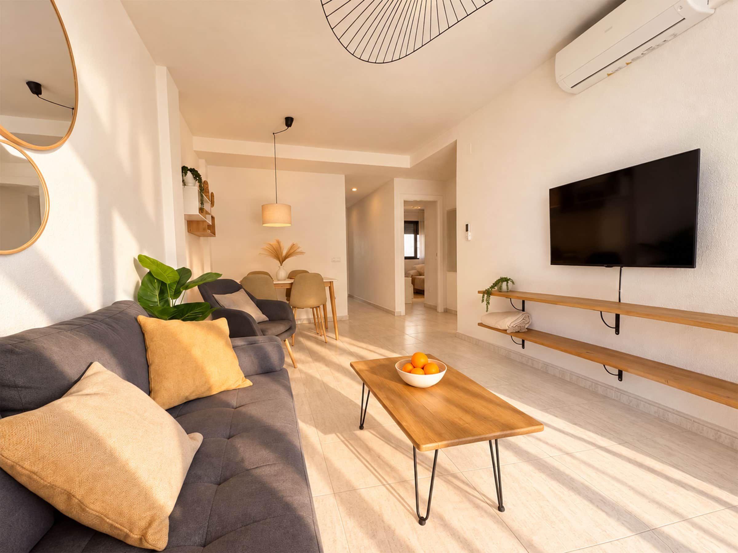 A modern living room with a sofa, a coffee table, a TV, and a dining area.