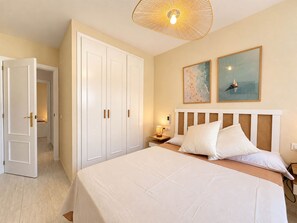 A hotel room with a large bed, a wardrobe, a nightstand with a lamp, and two wall art pieces. - 04 Caerulea - Sea View Apartment - Daimús (Daimús)