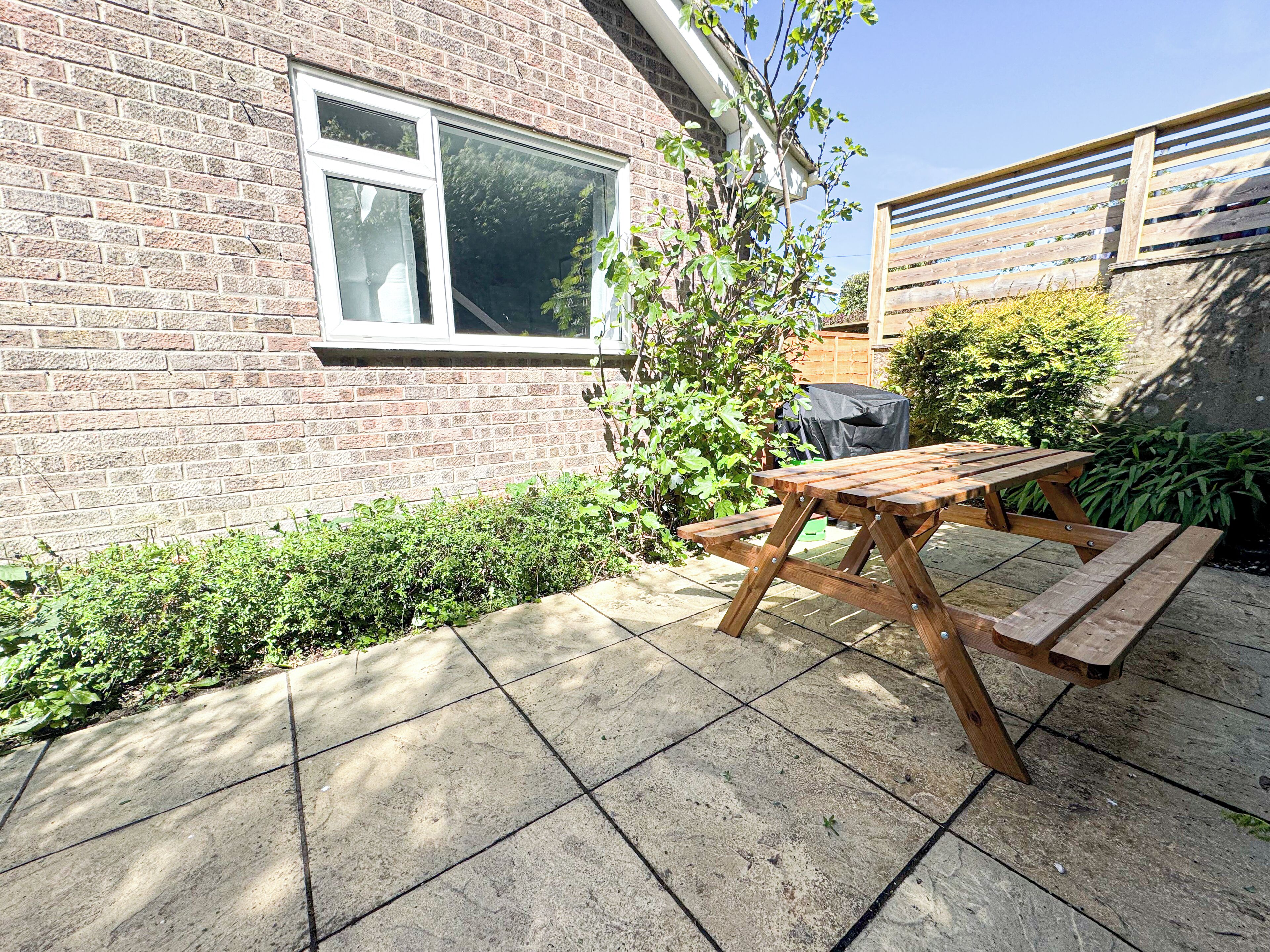 A brick house with a window, a wooden table, and a bench in the backyard.