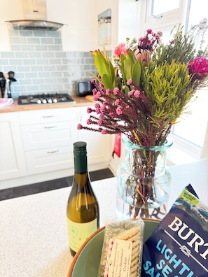 Una encimera de cocina con una botella de vino, un paquete de galletas y un florero con flores.