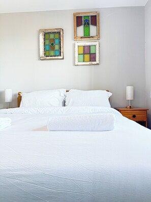 Una cama bien hecha con sábanas blancas, un cabecero de madera y dos mesitas de noche con lámparas.