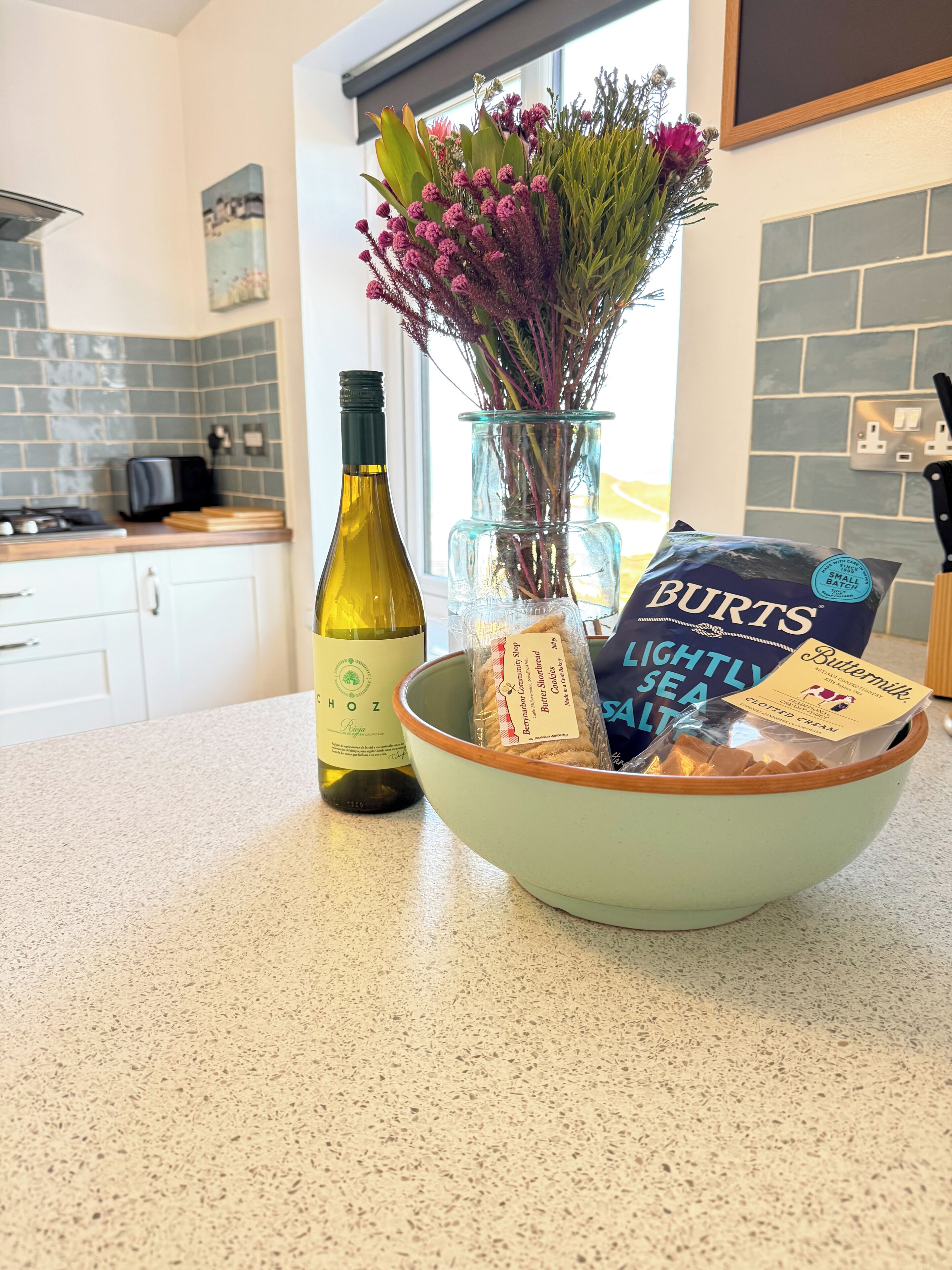 A kitchen counter with a wine bottle, a vase with flowers, and a bowl containing food items.