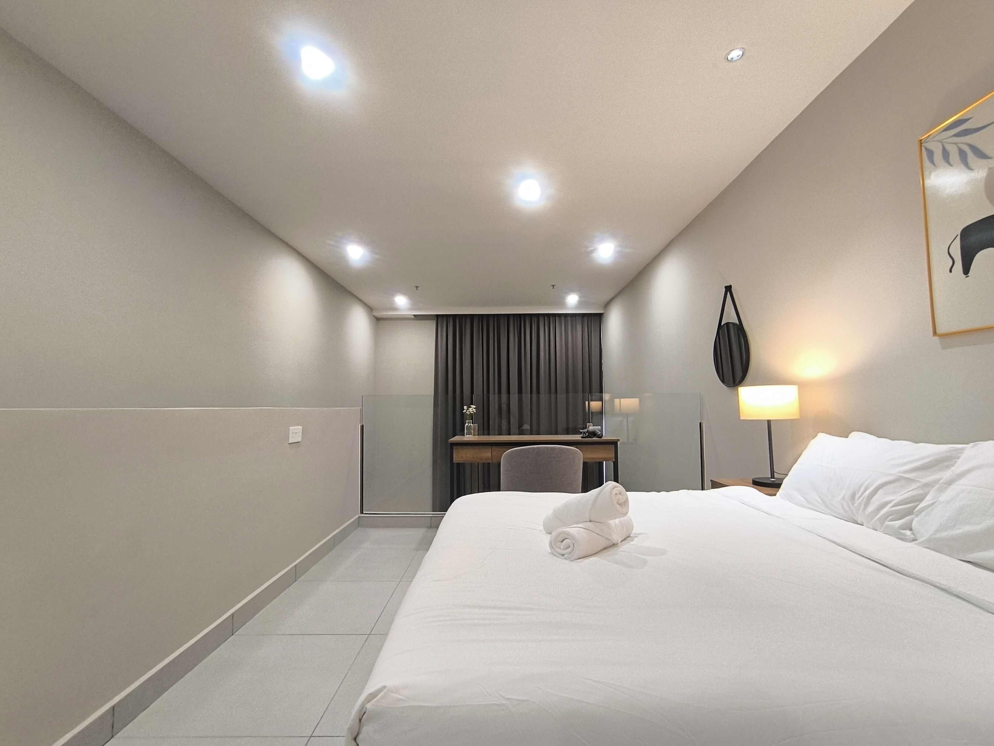 A hotel room with a large bed, a desk, a chair, a lamp, and a wall-mounted artwork.