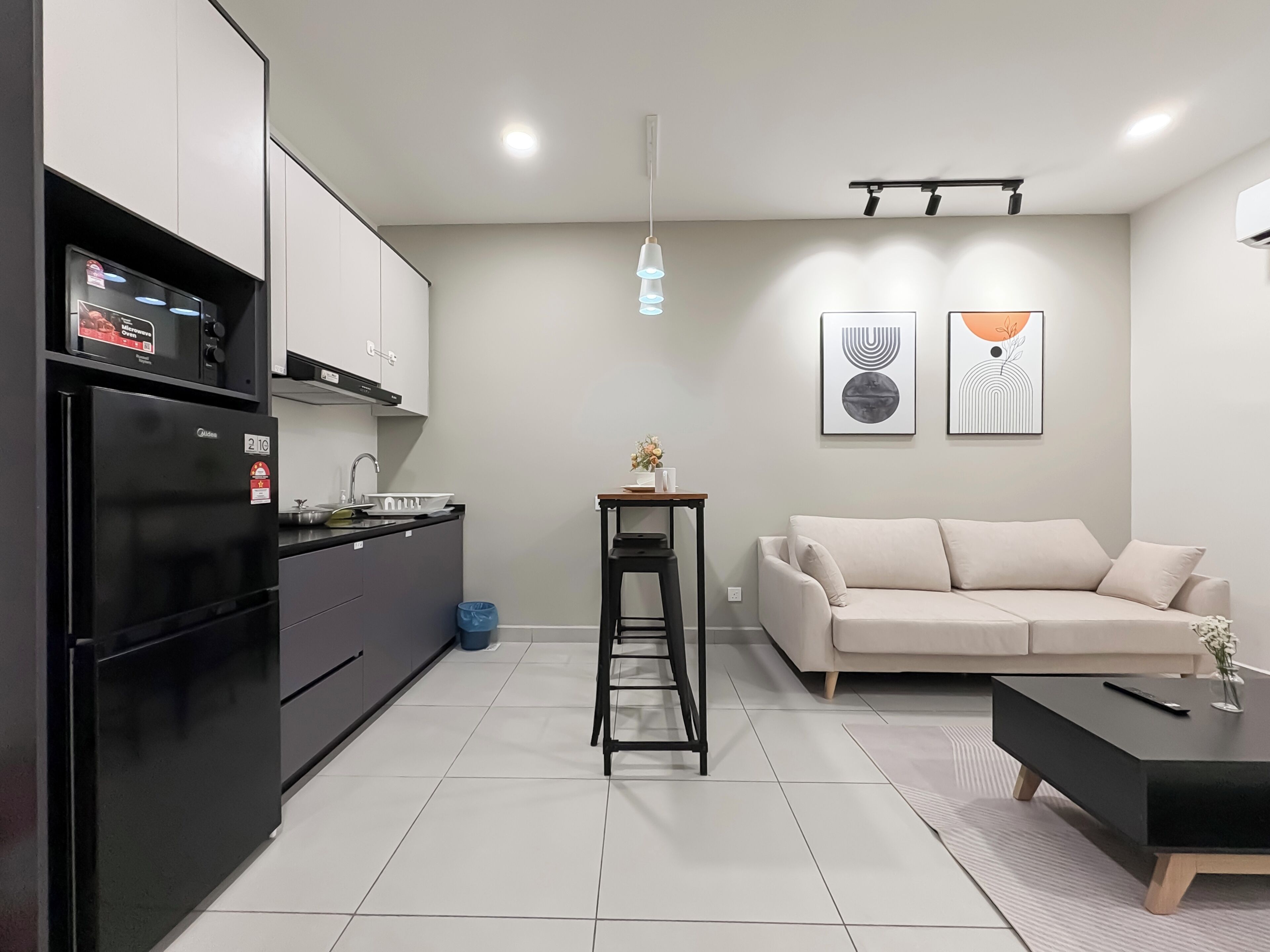 A modern kitchen with a built-in oven, a dining area with a sofa and a coffee table, and two abstract wall art pieces.
