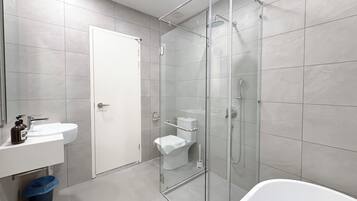 Un baño moderno con ducha de vidrio, lavamanos blanco y un inodoro.