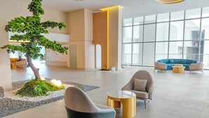 Een moderne lobby met een grote binnenboom, zithoek met sofa’s en fauteuils, en grote ramen.
