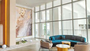 Een ruime lobby met een groot abstract schilderij, een blauwe bank en twee ronde tafels.