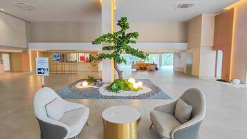A lobby with a reception desk, two grey armchairs, a small round table, and a decorative tree centerpiece.
