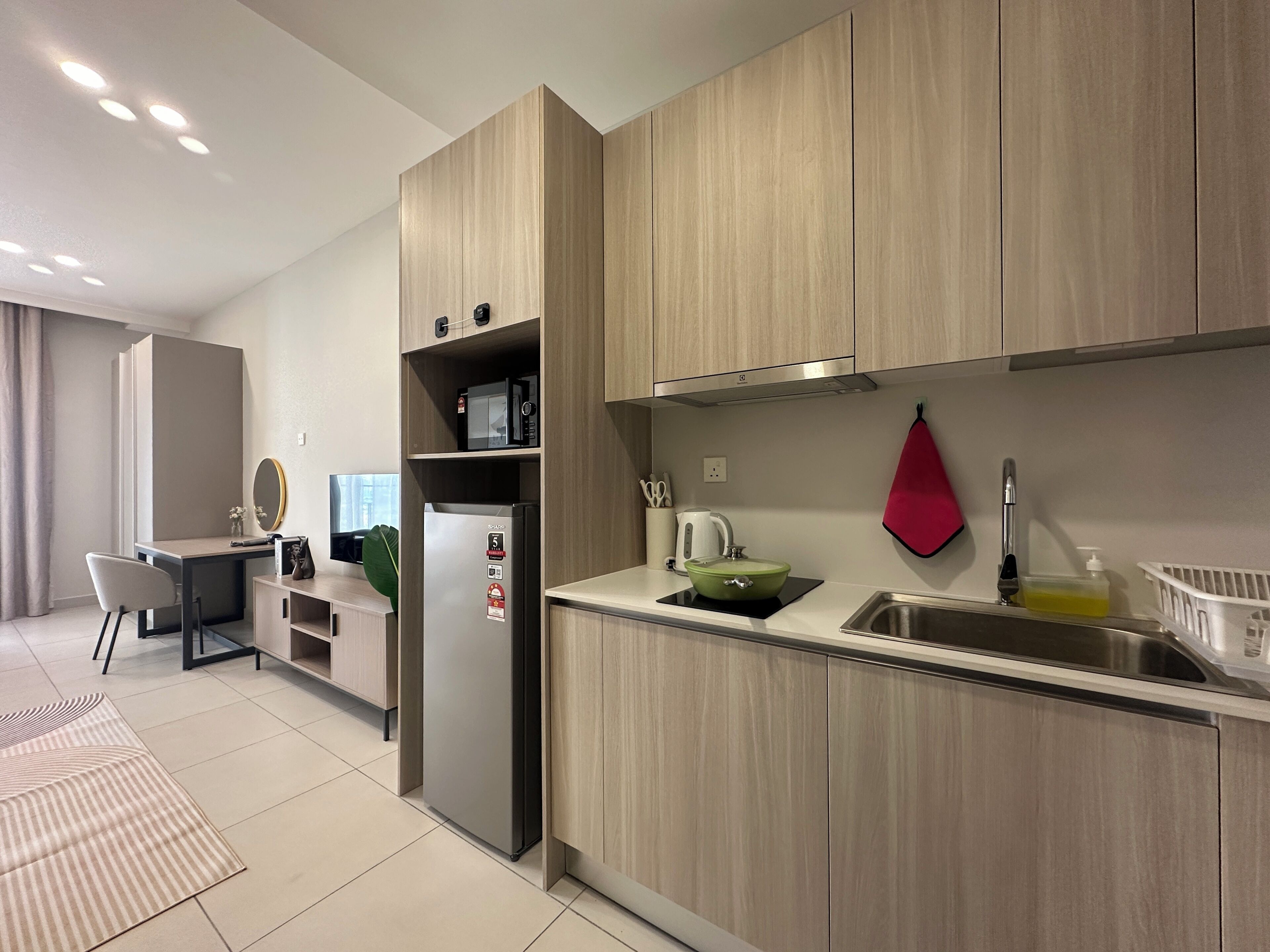 A modern kitchen with wooden cabinets, a built-in microwave, a stainless steel sink, and a red towel hanging on the wall.