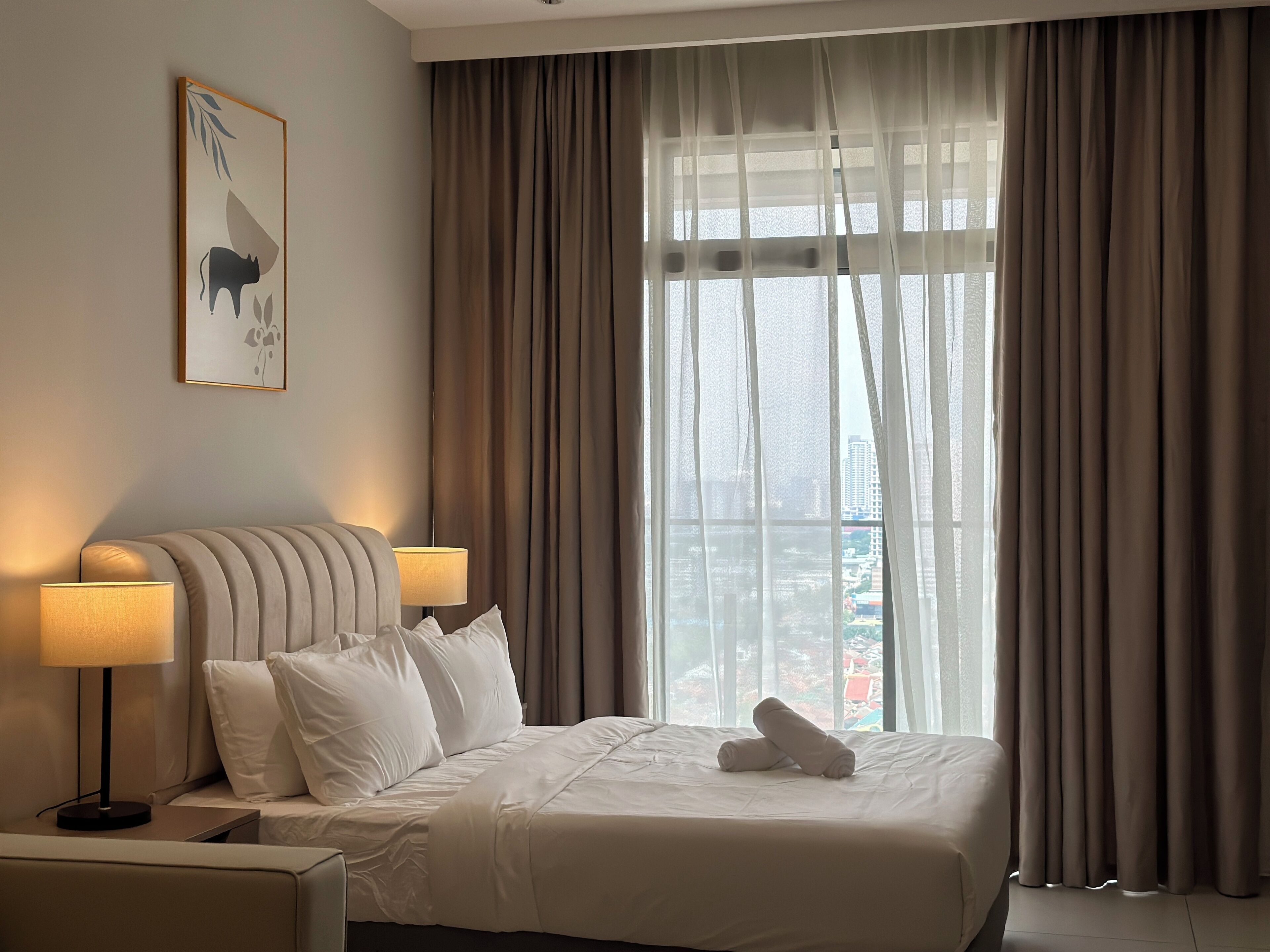 Habitación de hotel con cama, dos lámparas de noche, ventana con cortinas y vista a la ciudad.