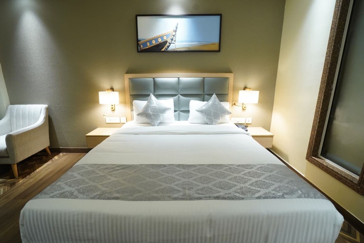 A hotel room with a bed, two bedside lamps, a chair, a painting on the wall, and a window.