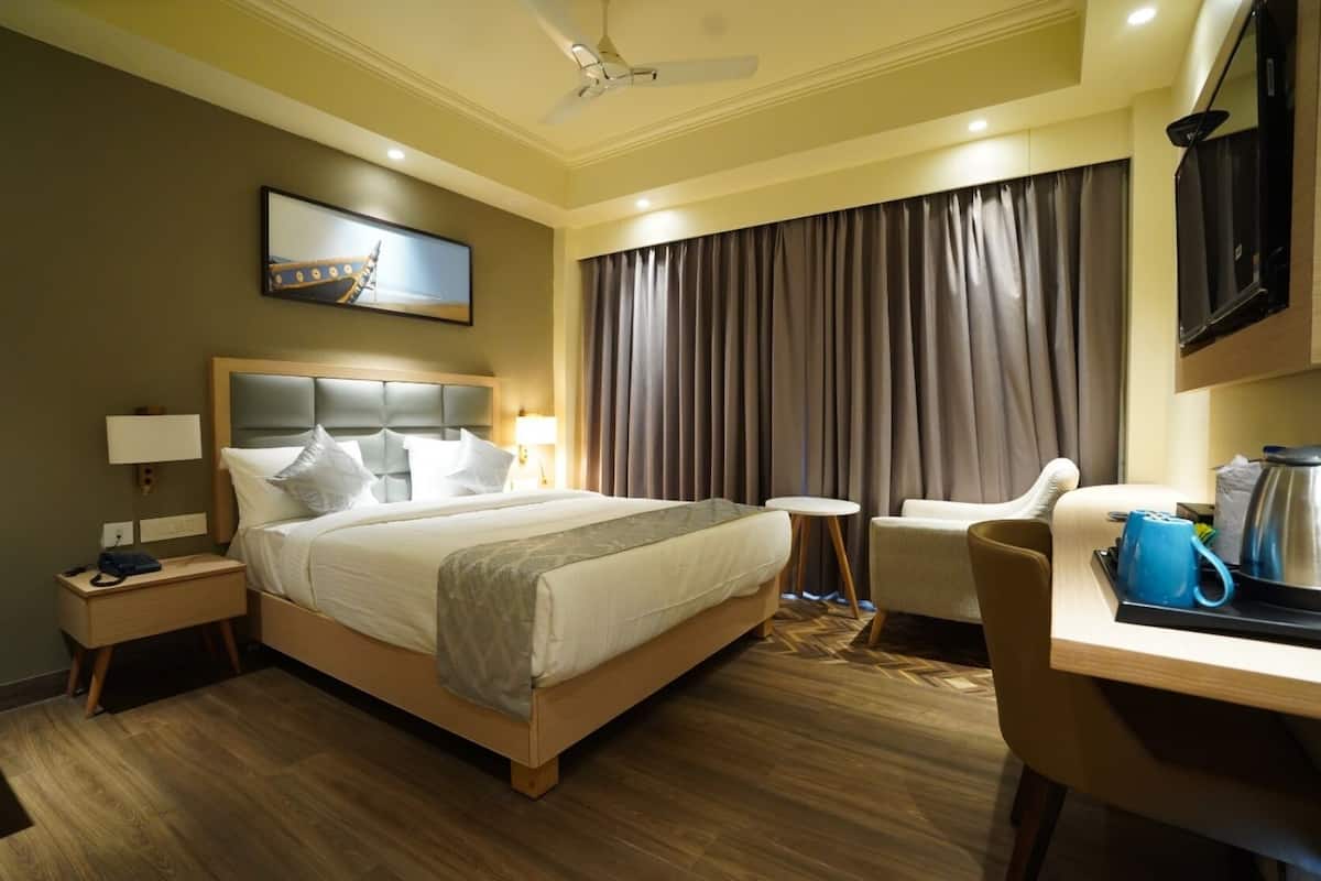 A hotel room with a bed, a desk, a chair, a television, and a painting on the wall.