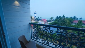 A balcony with a chair, a decorative railing, and a view of a lighthouse and buildings. - The Sea Valley Heights Puri (Puri)
