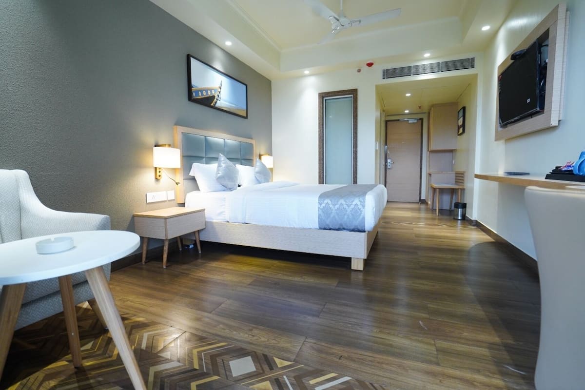 A hotel room with a bed, bedside tables, a chair, a desk, a TV, and a door leading to another room.