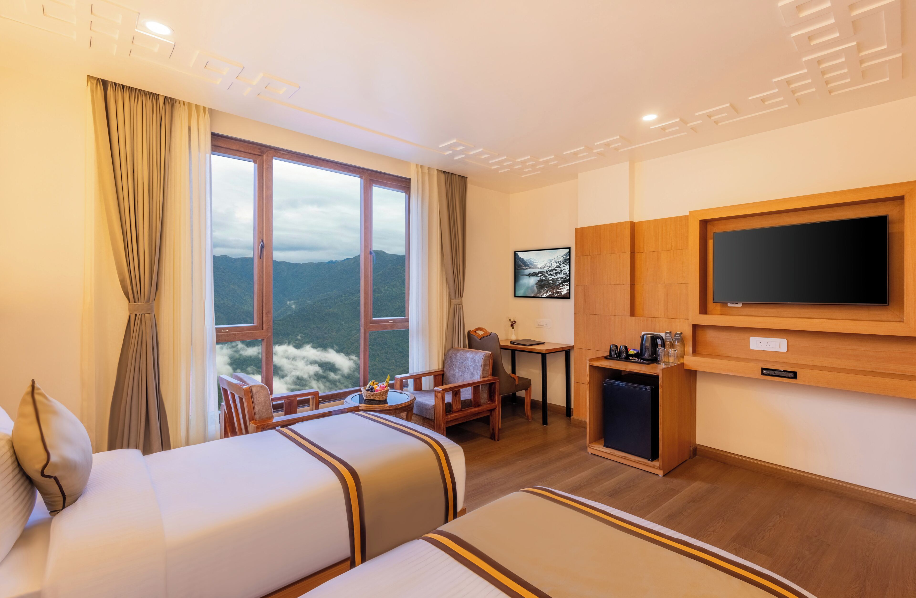 Habitació d'hotel amb dos llits, televisió, escriptori, cadira i vista a les muntanyes.