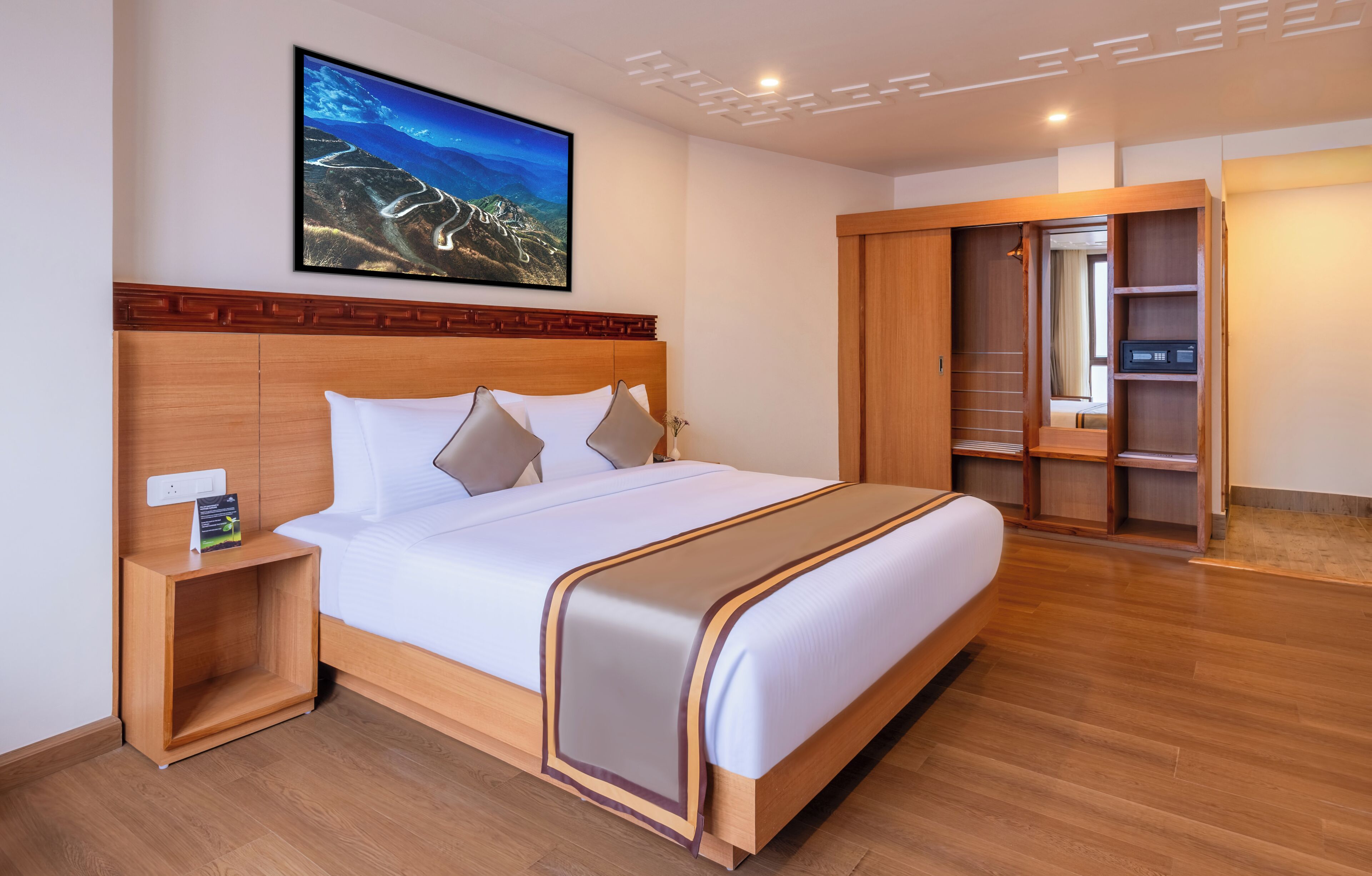 Une chambre d’hôtel avec un grand lit, une tête de lit en bois, une table de chevet, une commode, une armoire et un tableau encadré au mur.