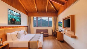 Habitación de hotel con cama, sofá, escritorio, televisor y una ventana grande con vistas a la montaña.