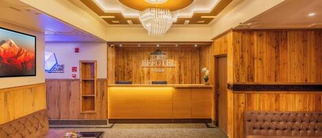 A hotel reception area with a wooden reception desk, a chandelier, a sofa, and a coffee table with flowers.