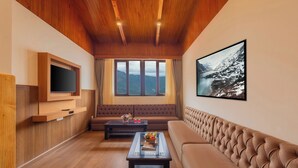 Sala de estar con techo de madera, un ventanal con vistas a la montaña, un sofá, una mesa de centro y un televisor de pantalla plana montado en la pared.