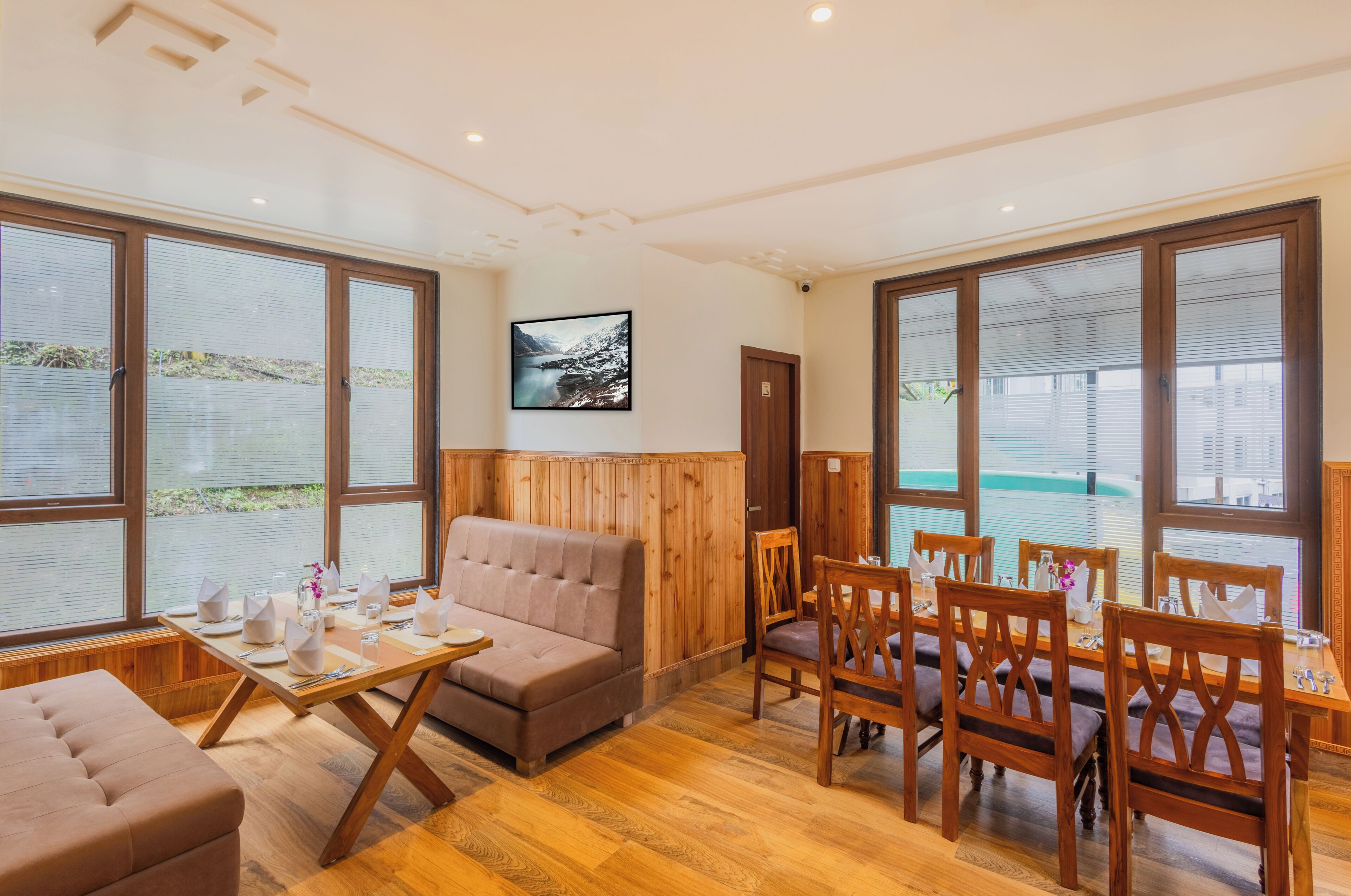 A room with a sofa, dining table, chairs, large windows, and a framed picture on the wall.