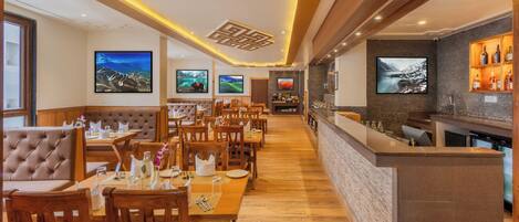 Un restaurante con varias mesas para comer y cabinas, una zona de bar y televisores empotrados mostrando imágenes panorámicas.