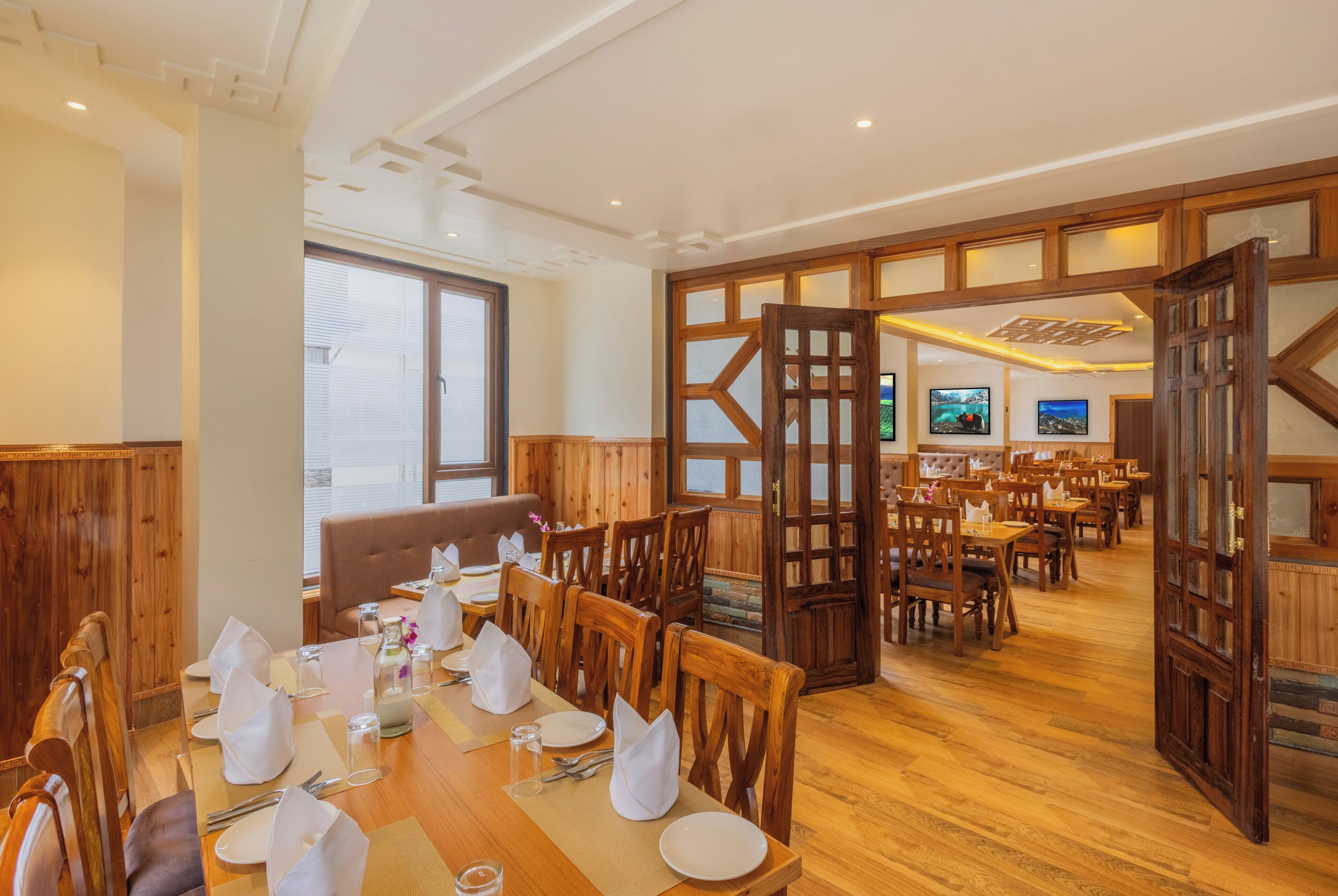 Un restaurant avec des meubles en bois, un plafond haut et une vue sur l’extérieur grâce à une porte ouverte.