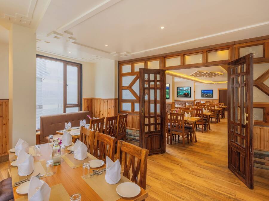 Un restaurant avec des meubles en bois, un plafond haut et une vue sur l’extérieur grâce à une porte ouverte.