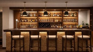 Zona de bar con mostrador de madera, varias estanterías llenas de botellas y taburetes.