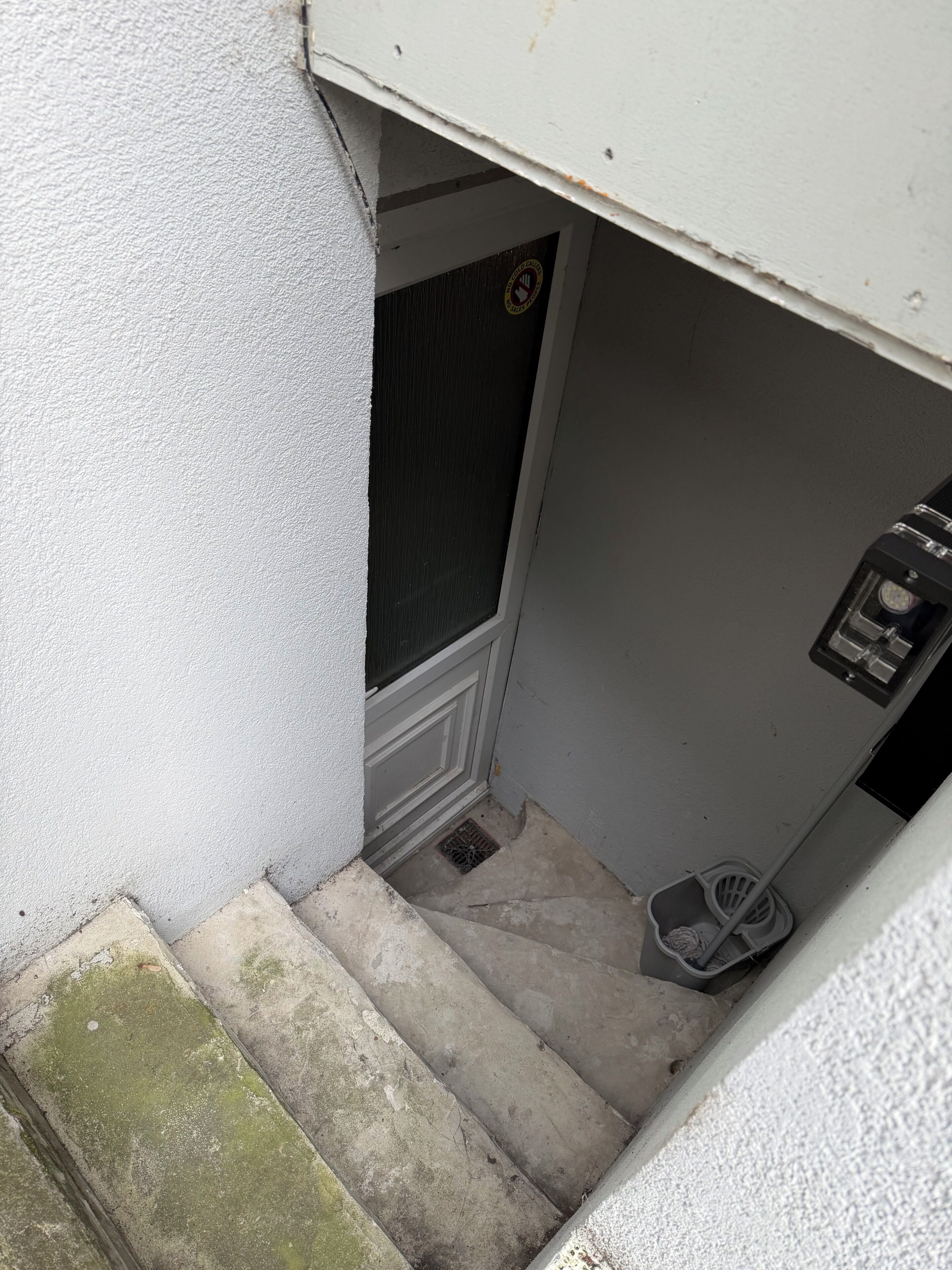Un escalier menant à une porte dotée d’une serrure de sécurité, une petite poubelle et une grille métallique au bas de l’escalier.