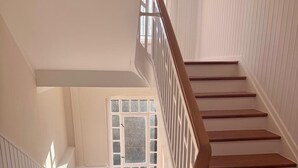 A staircase with wooden steps and white railings, leading to a landing with a window.