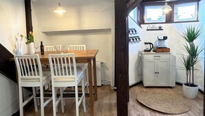 A dining area with a wooden table and white chairs, a coffee station with a coffee machine, and a potted plant.