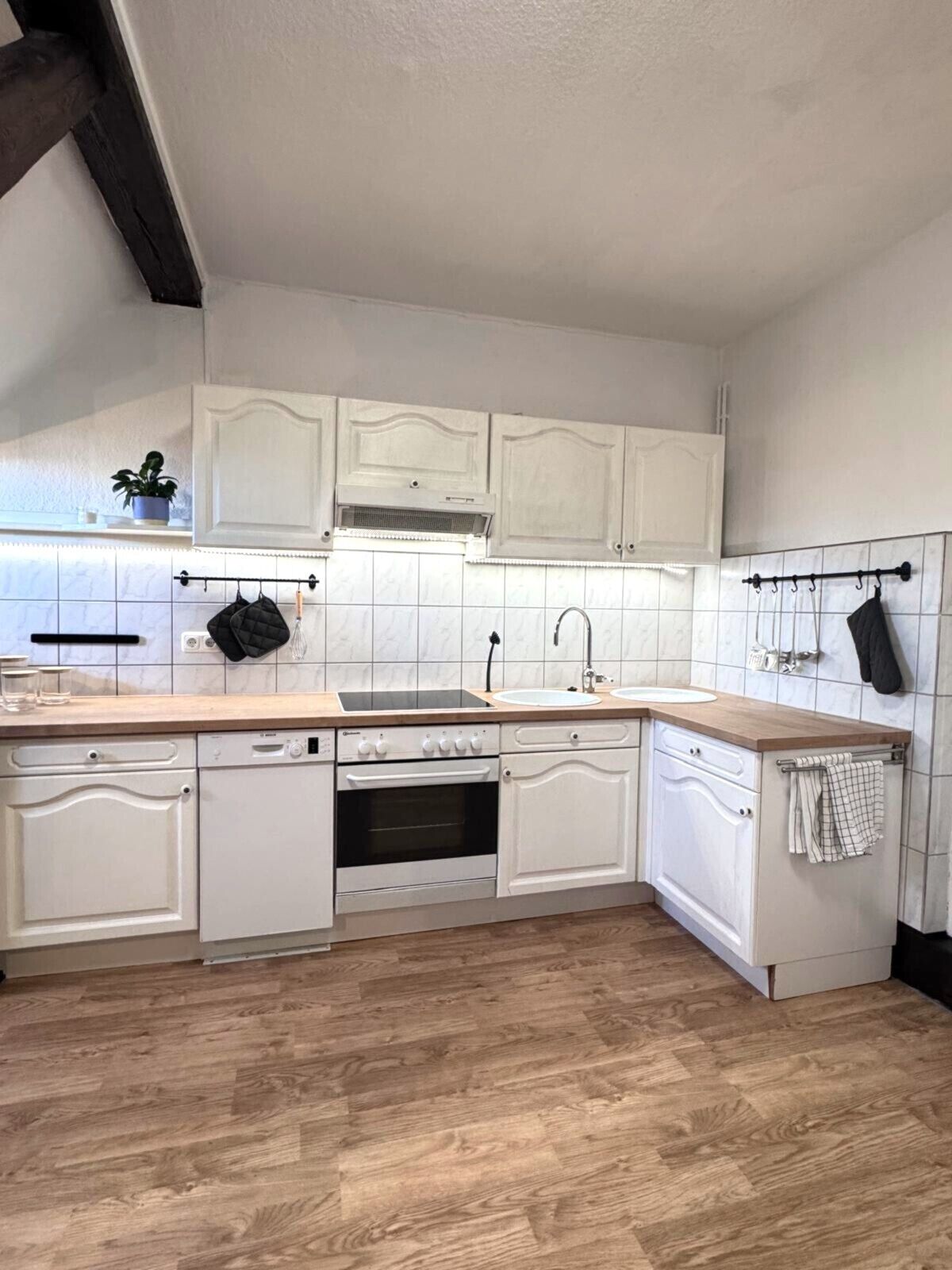 A kitchen with white cabinetry, a wooden countertop, a dishwasher, an oven, and a sink.