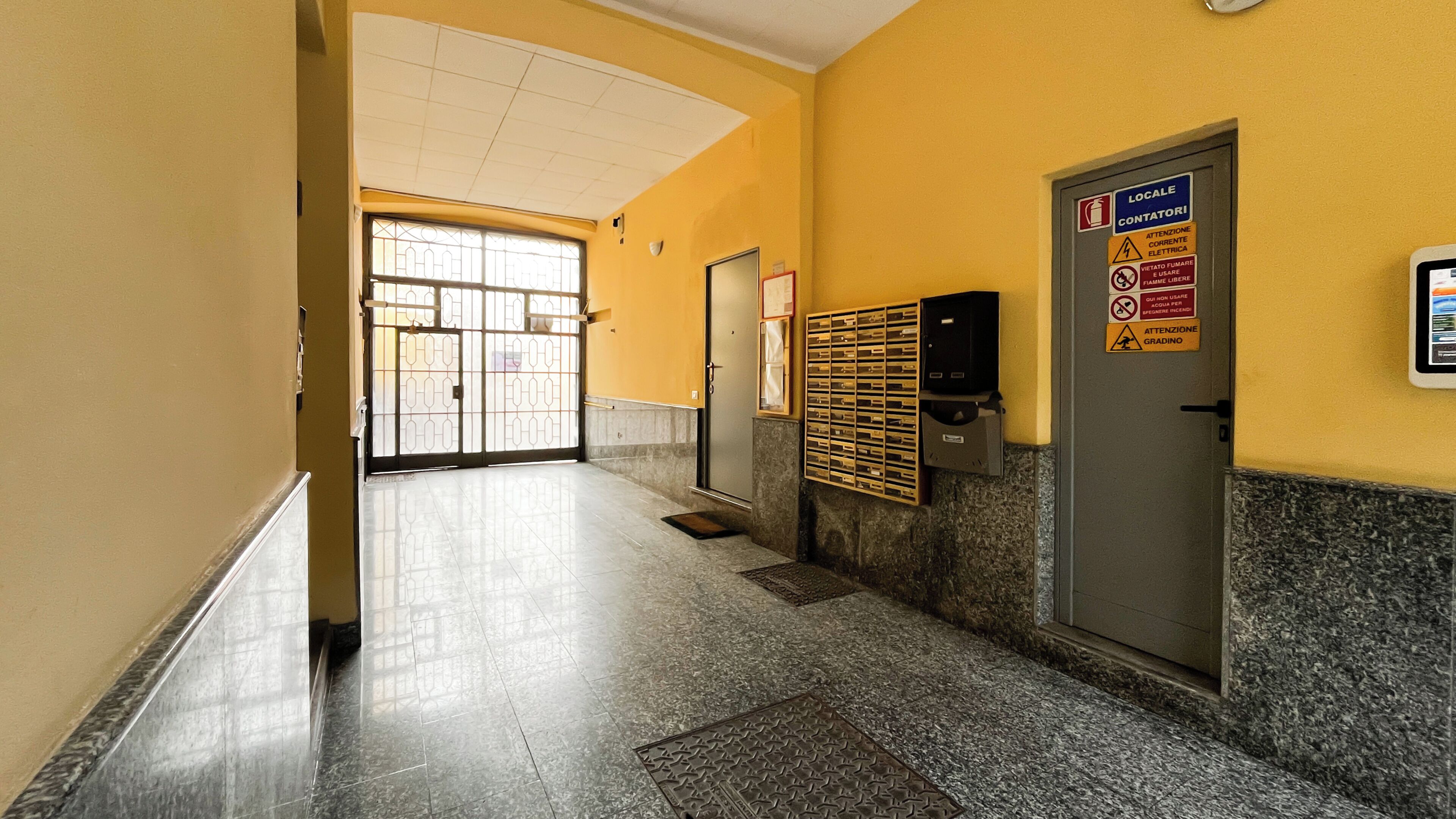 A hallway with a tiled floor, a door with a sign, and a mailbox.