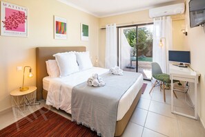Ein Hotelzimmer mit Bett, Schreibtisch, Stuhl, Klimaanlage und einem fensterbepflanzten Fenster.
