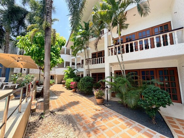 A courtyard with a tiled walkway, palm trees, potted plants, and outdoor seating. - Cozy Ground Floor Suite with Shared Pool (Tambon Patong)