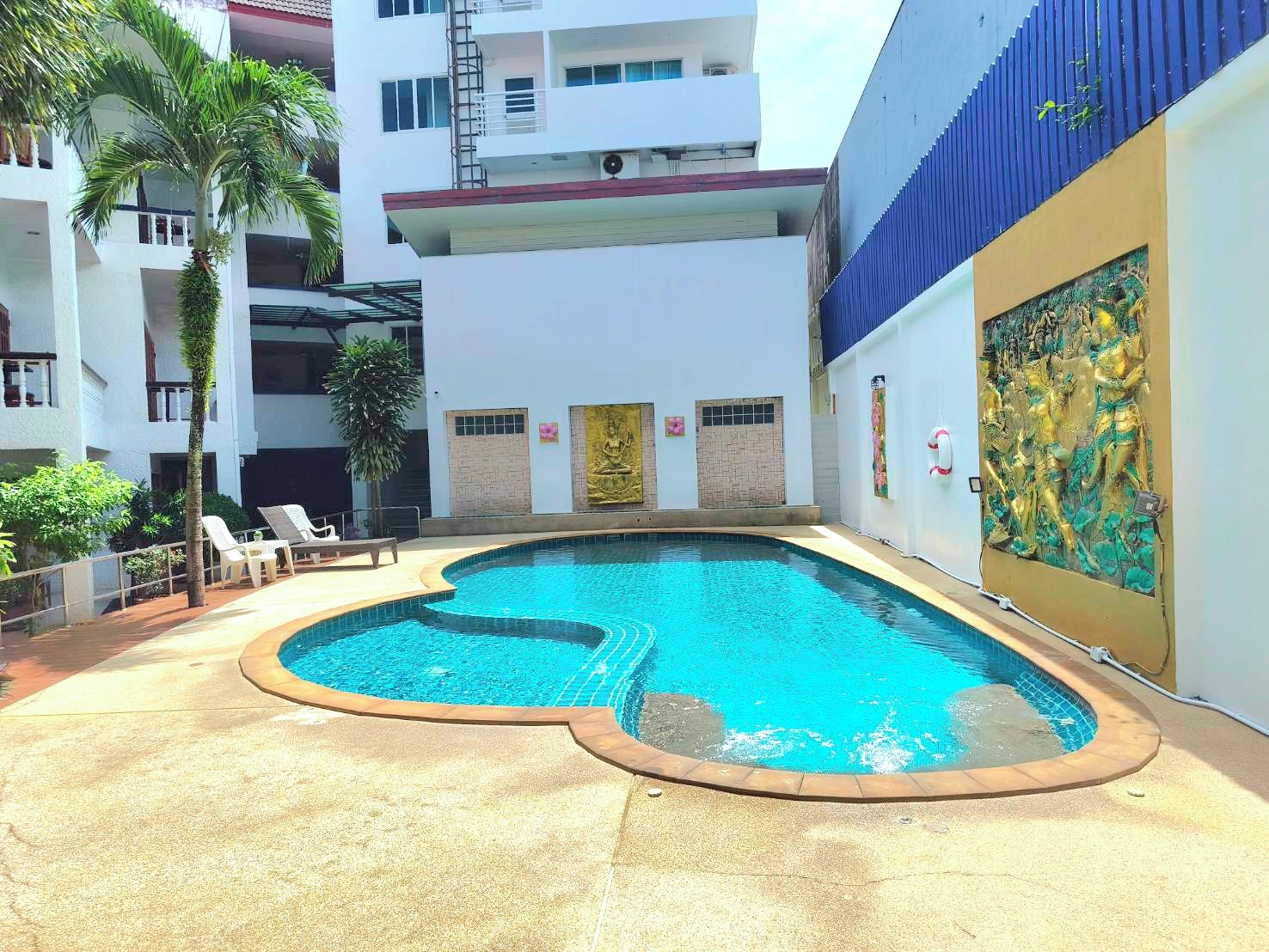 A swimming pool with a curved edge, surrounded by lounge chairs and palm trees.